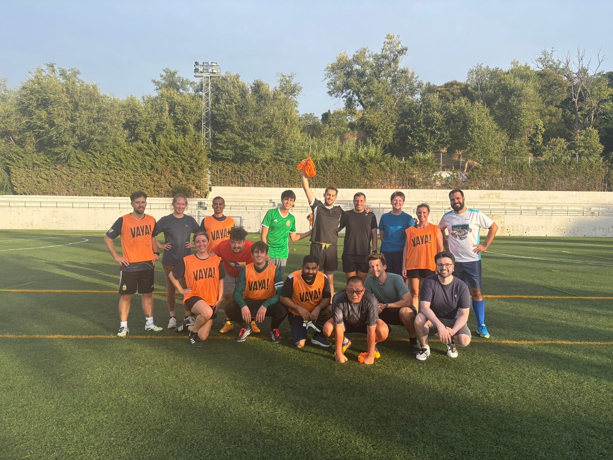 Keep Calm Community Barcelona Friday football group photo, mixed team wearing orange Vaya Sports bibs on an outdoor turf pitch
