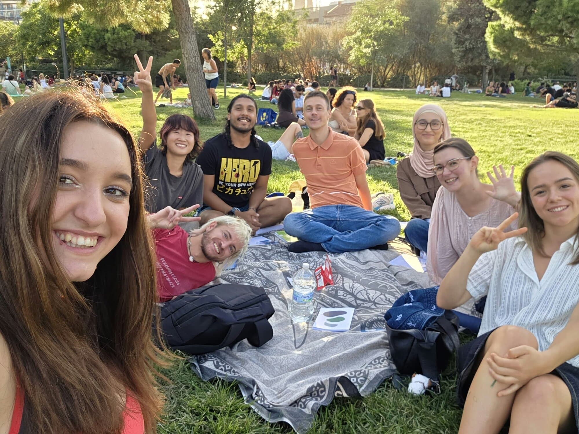 Keep Calm Community Barcelona language exchange group smiling and waving together on a picnic blanket in a sunny park