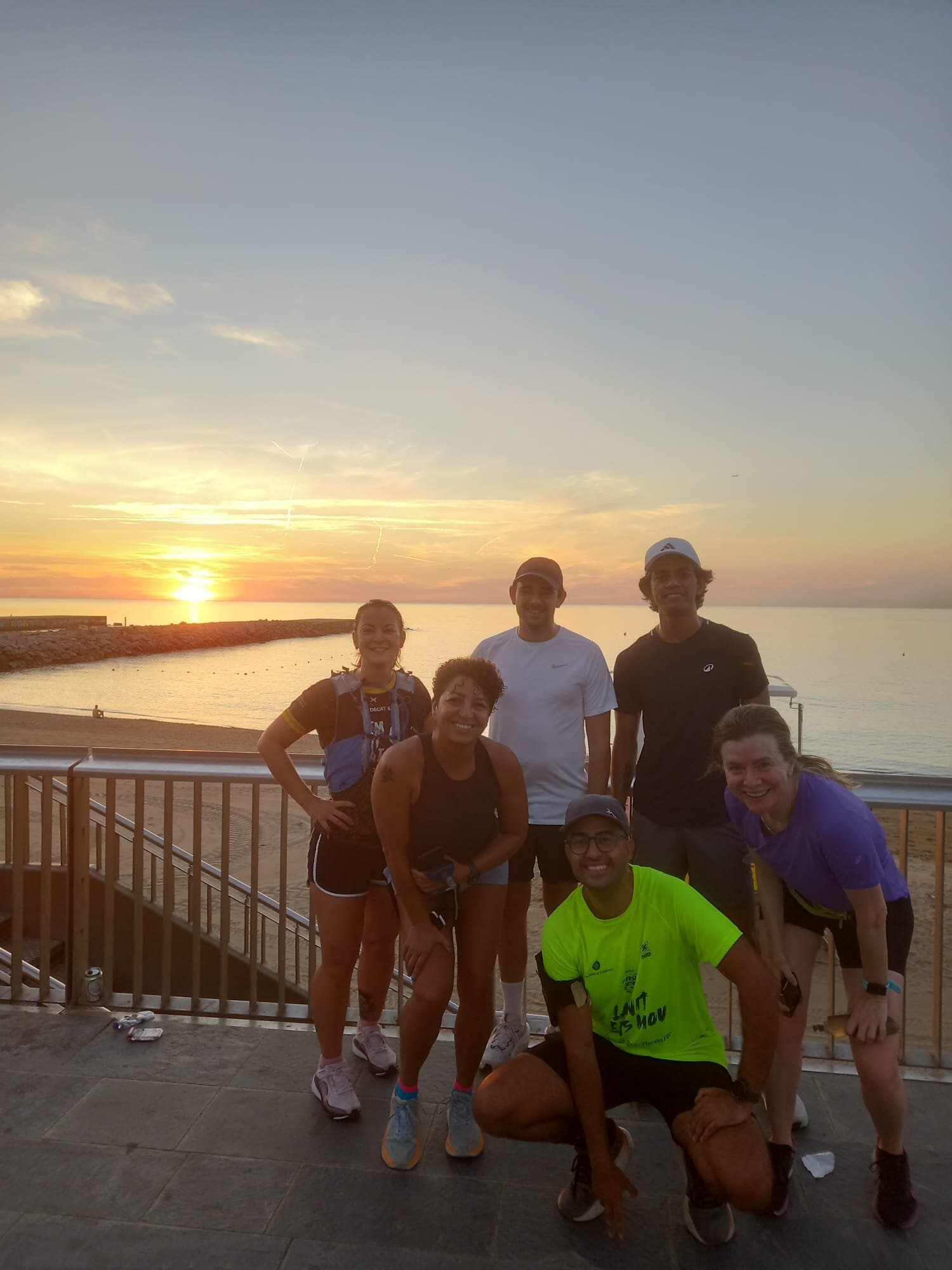 Keep Calm Community Barcelona runners smiling together on a beachfront promenade after a sunrise run
