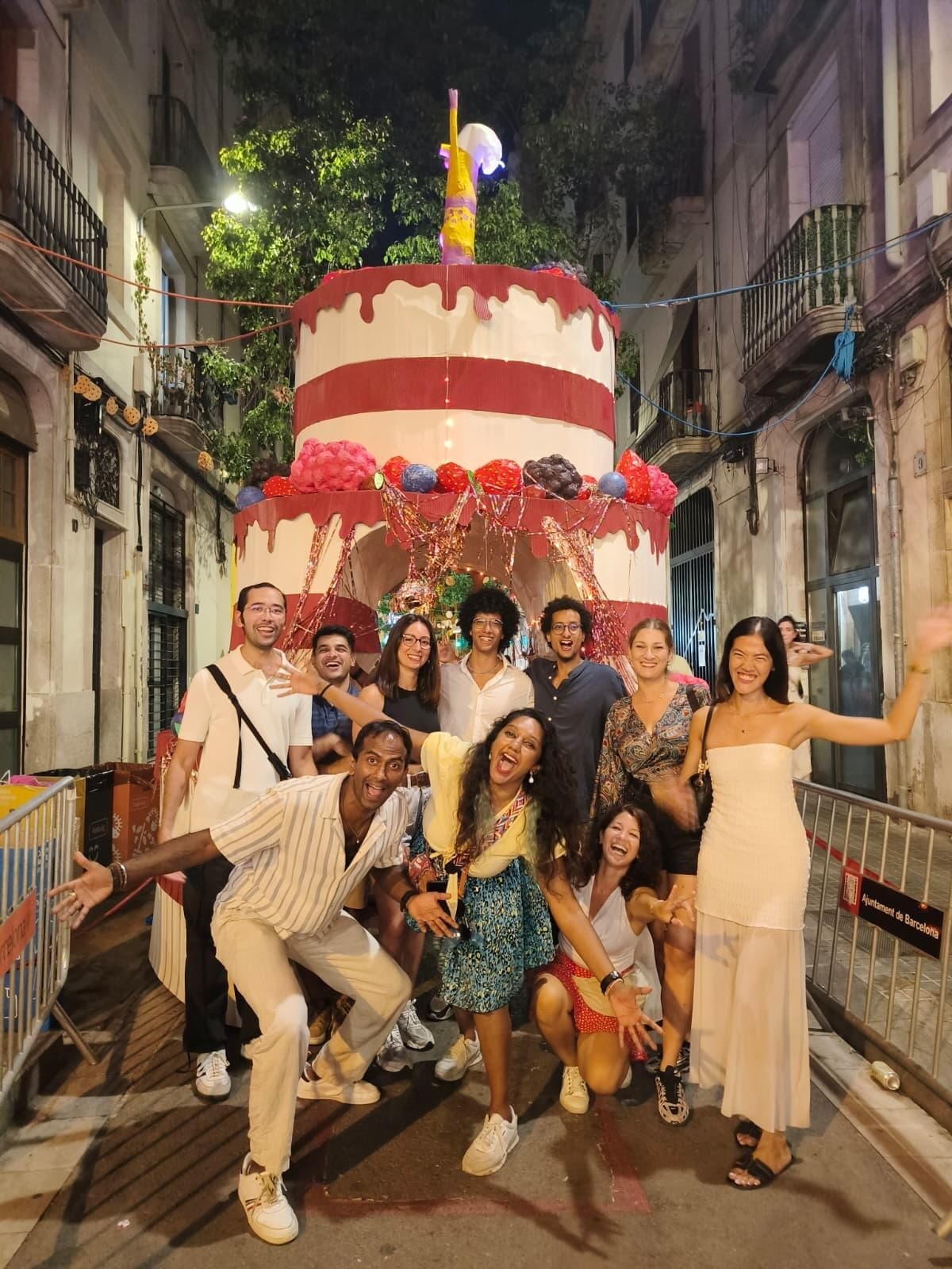 Keep Calm Community Barcelona group posing at night in front of a giant decorated cake street display during the Sants neighbourhood festa major